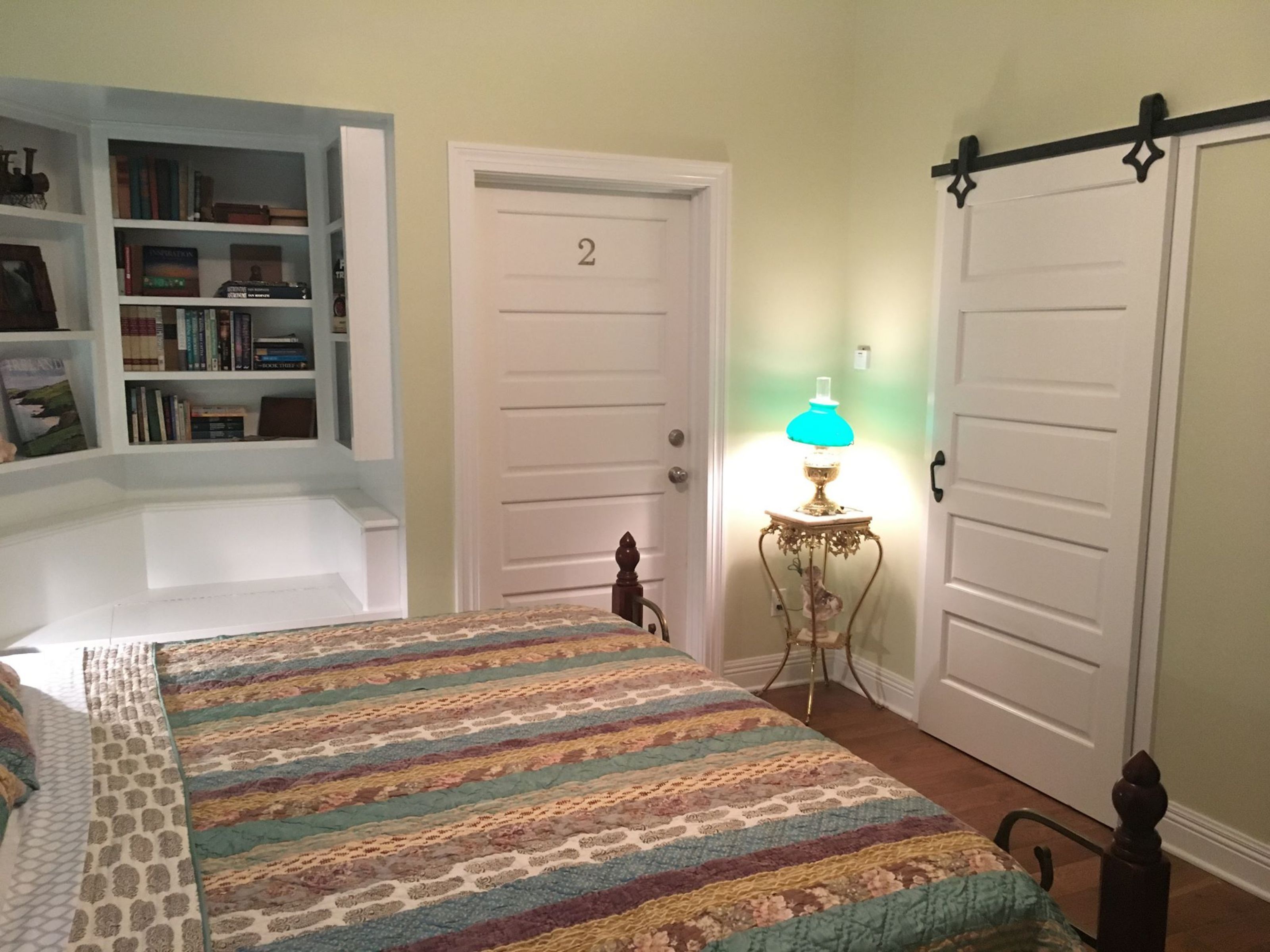 A bedroom with a bed, a bookshelf, a door labeled '2', and a lamp.