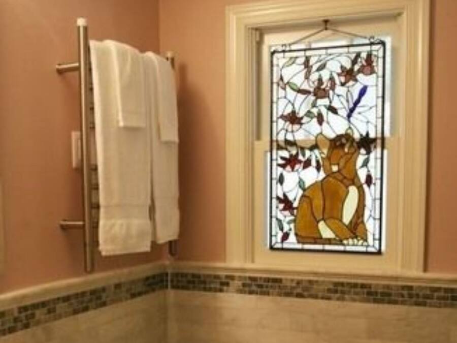 A bathroom with a toilet, a sink, a towel rack, and a stained glass window.