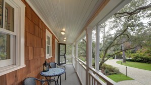 A covered porch with a wooden wall, a small table with chairs, and a view of a garden with a pathway. - The Grey Owl Inn (St. Simons Island)