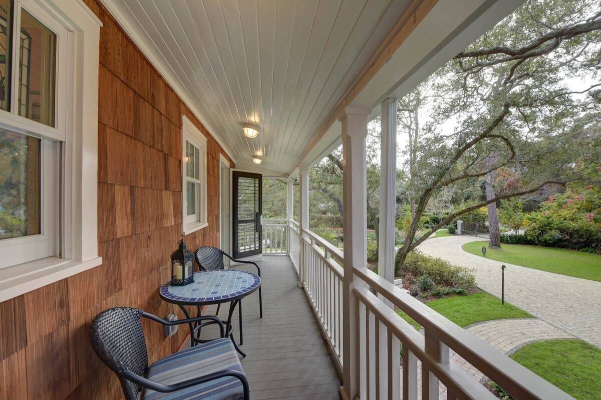 A covered porch with a wooden wall, a small table with chairs, and a view of a garden with a pathway.
