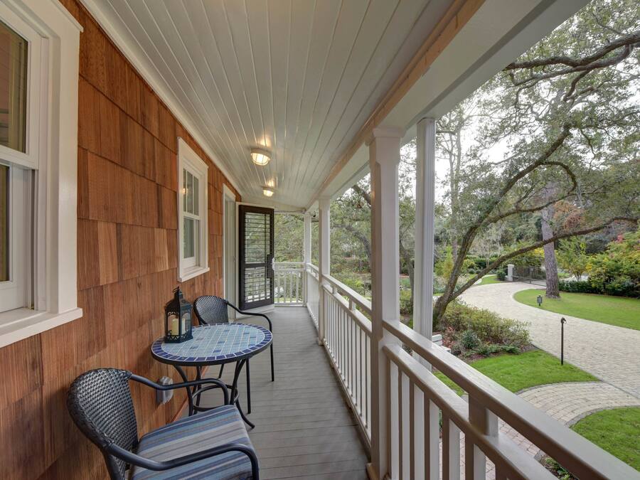 A covered porch with a wooden wall, a small table with chairs, and a view of a garden with a pathway.