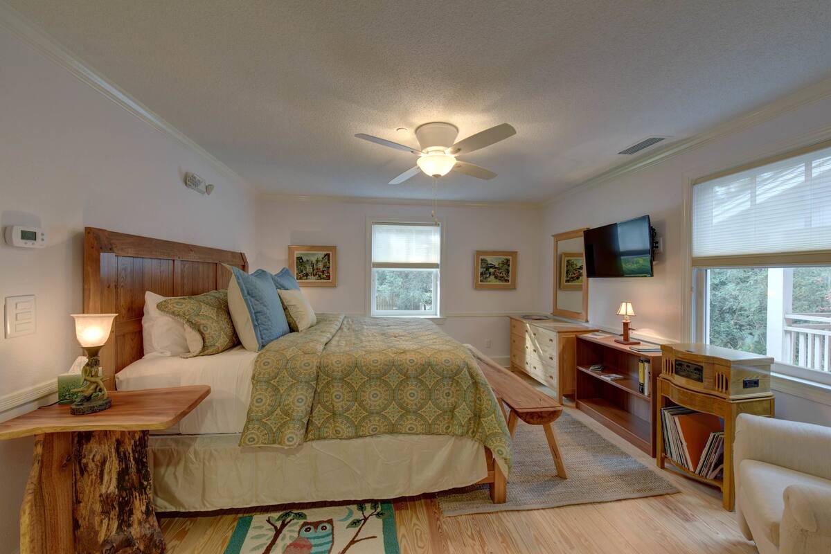 A bedroom with a bed, bedside table, lamp, wooden nightstand, bookshelf, and a ceiling fan.
