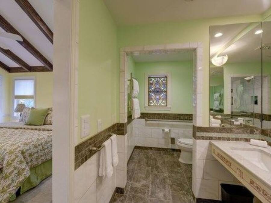 Een slaapkamer met een bed, een badkamer met een bad en een grote spiegel.
