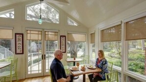 A dining area with a table and chairs, large windows, and a view of the outdoors. - The Grey Owl Inn (St. Simons Island)