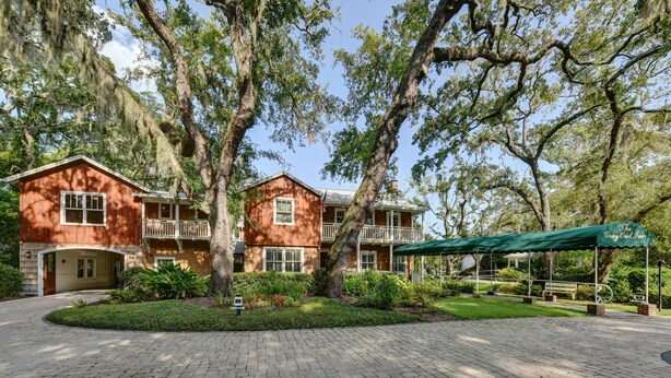 A two-story building with a brick facade, large trees, and a paved walkway. - The Grey Owl Inn (St. Simons Island)
