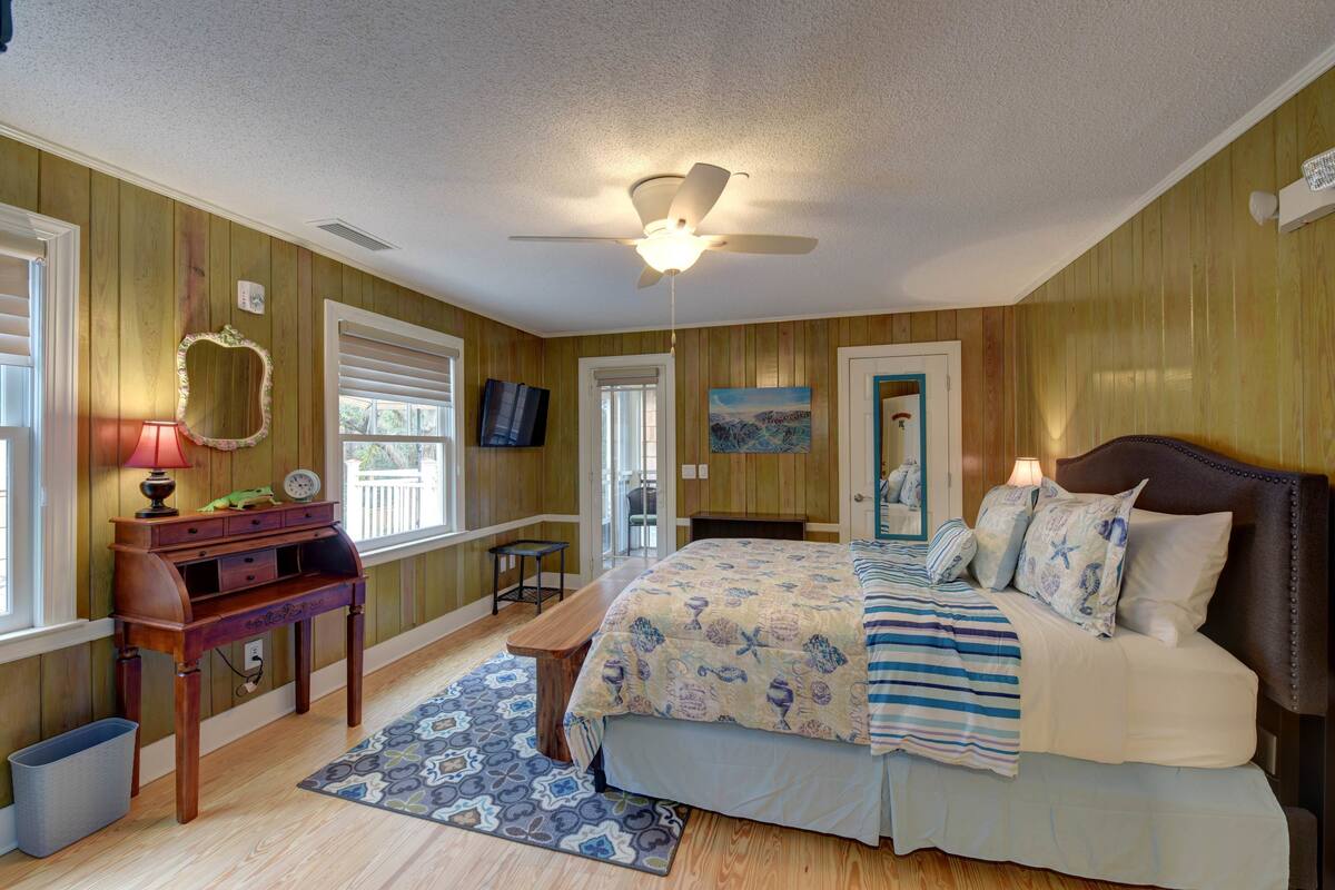 A bedroom with a bed, bedside lamps, a wooden nightstand, a mirror, and a ceiling fan.