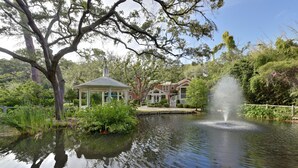 A tranquil pond with a gazebo and a fountain, surrounded by lush greenery and a building in the background. - The Grey Owl Inn (St. Simons Island)