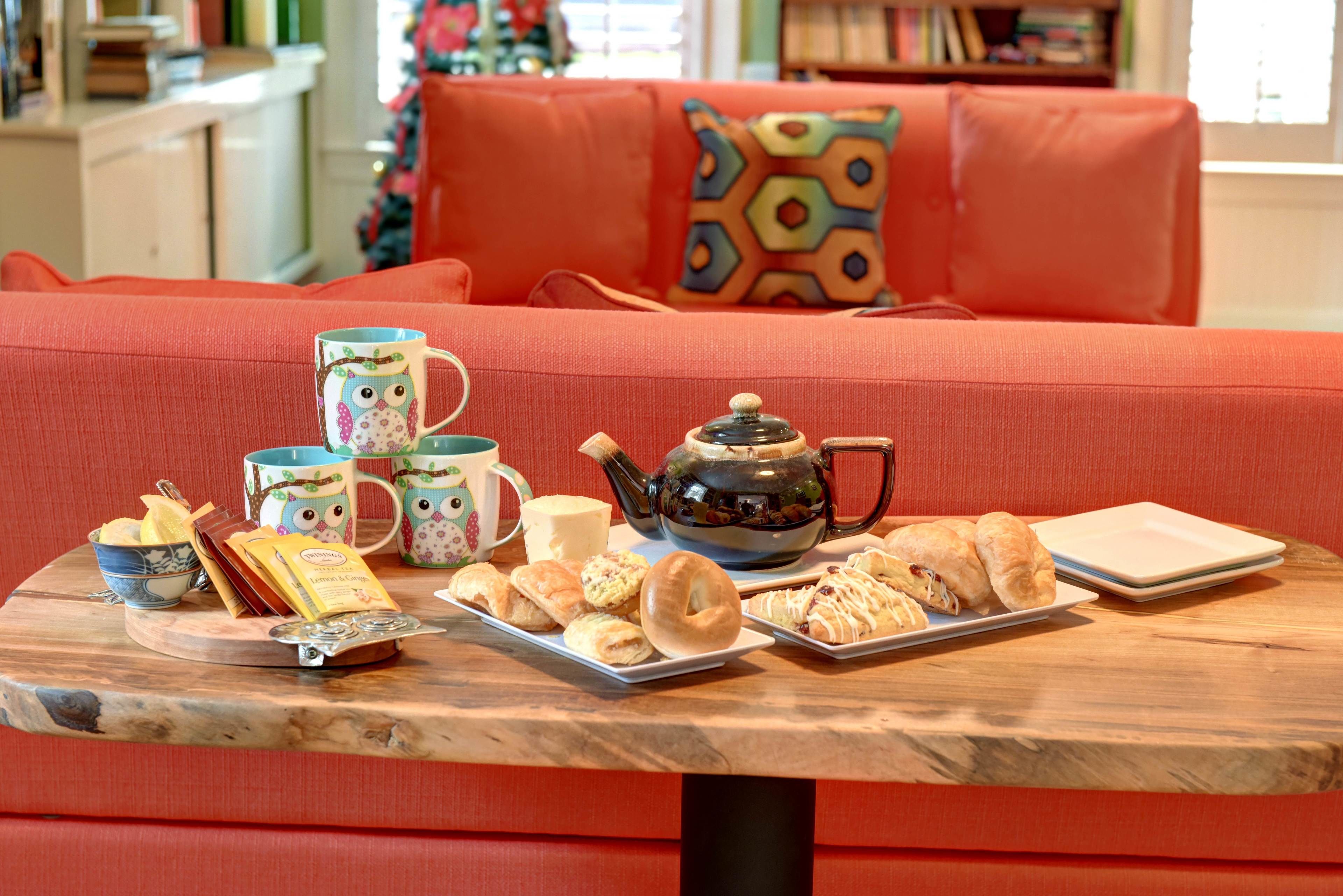 A cozy living room with a red sofa, a wooden coffee table with pastries, a teapot, and a mug.