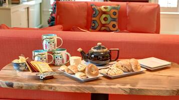 A cozy living room with a red sofa, a wooden coffee table with pastries, a teapot, and a mug.