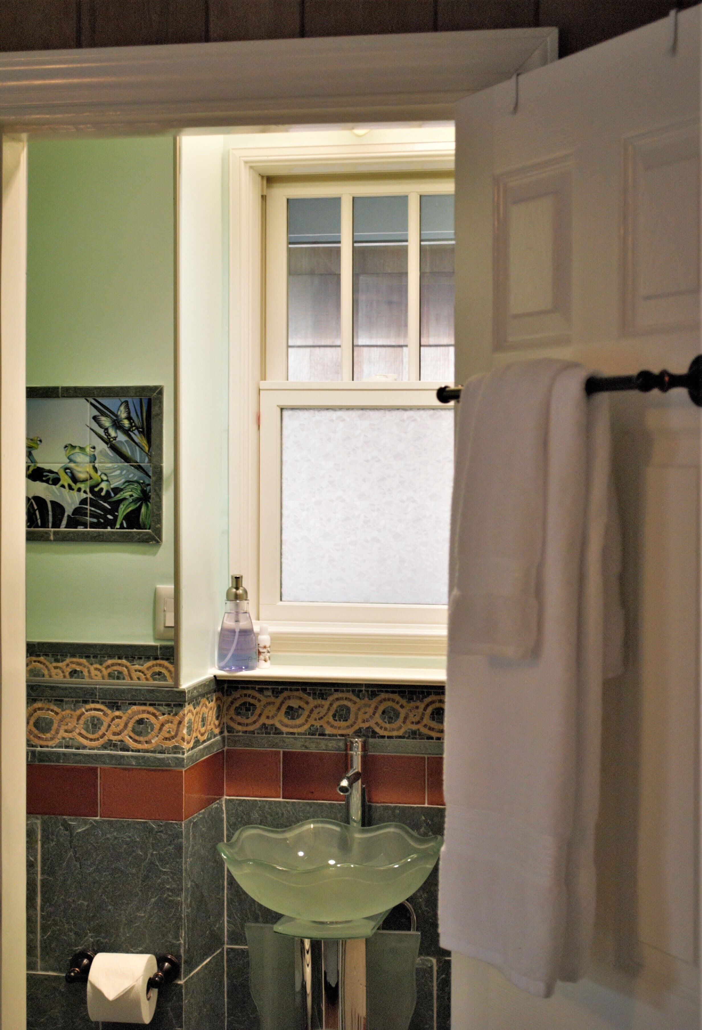 A bathroom with a glass sink, a window, and a towel rack.