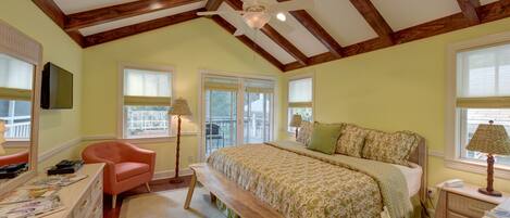 A bedroom with a large bed, a desk, a chair, a bench, and a ceiling fan.