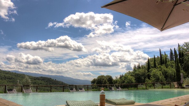 Zona junto a la piscina con sillones, una botella y vistas a montañas y árboles.