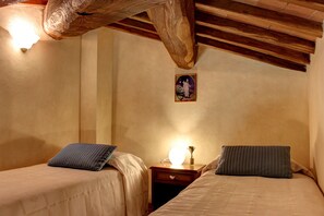 Una habitación acogedora con dos camas, vigas de madera, una mesita de noche con una lámpara y un cuadro enmarcado en la pared.