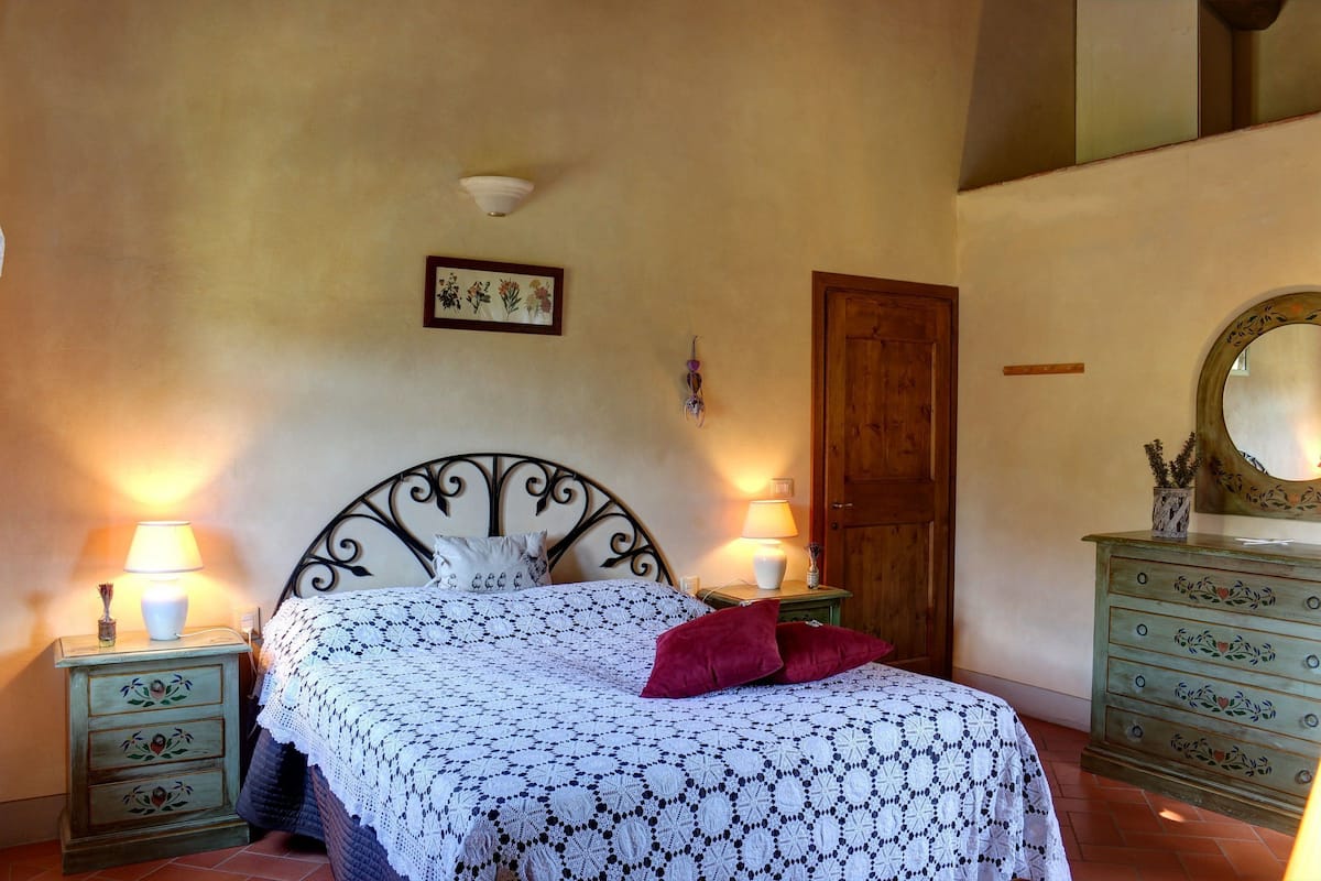 Ein Schlafzimmer mit einem Bett, zwei Nachttischen mit Lampen, einer Kommode, einem Spiegel und einem gerahmten Bild an der Wand.