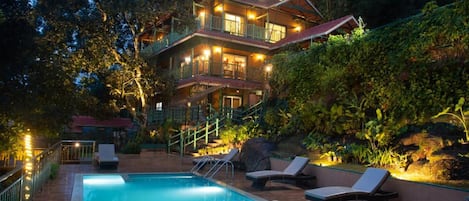 A multi-story building with a pool and lounge chairs.