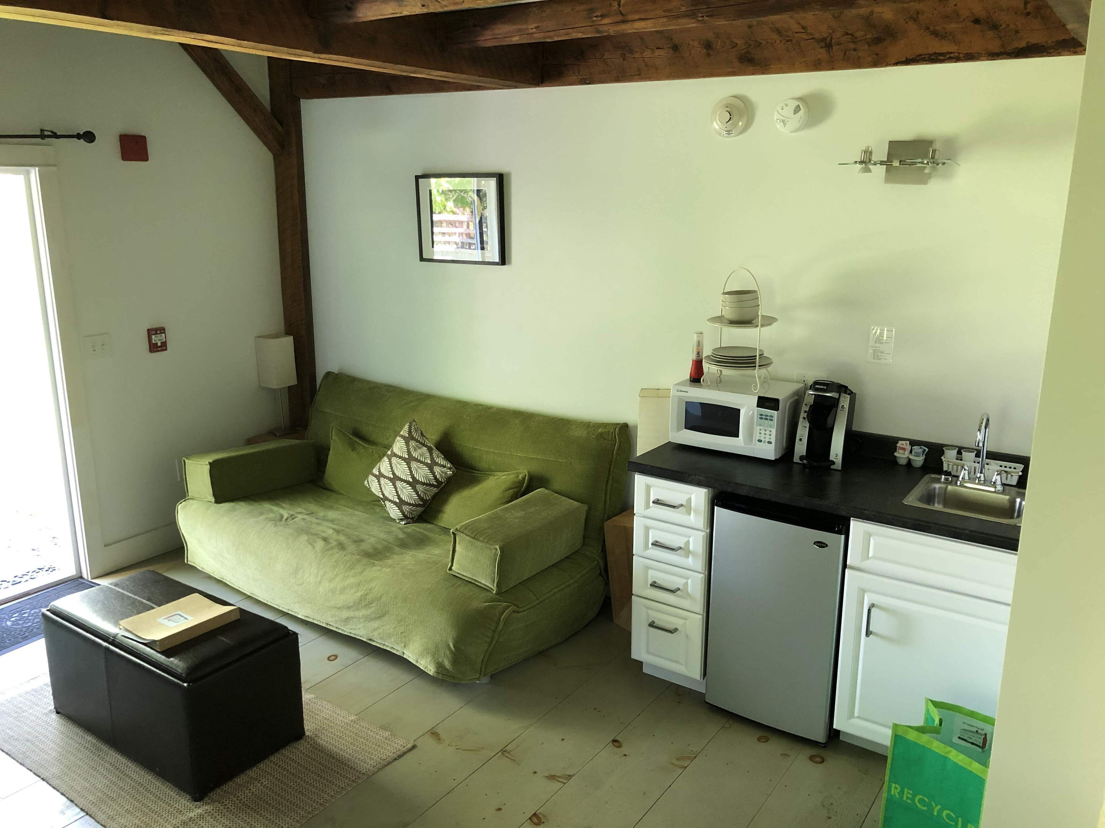 Un espace de vie compact comprenant un canapé vert, une petite kitchenette et un meuble blanc.