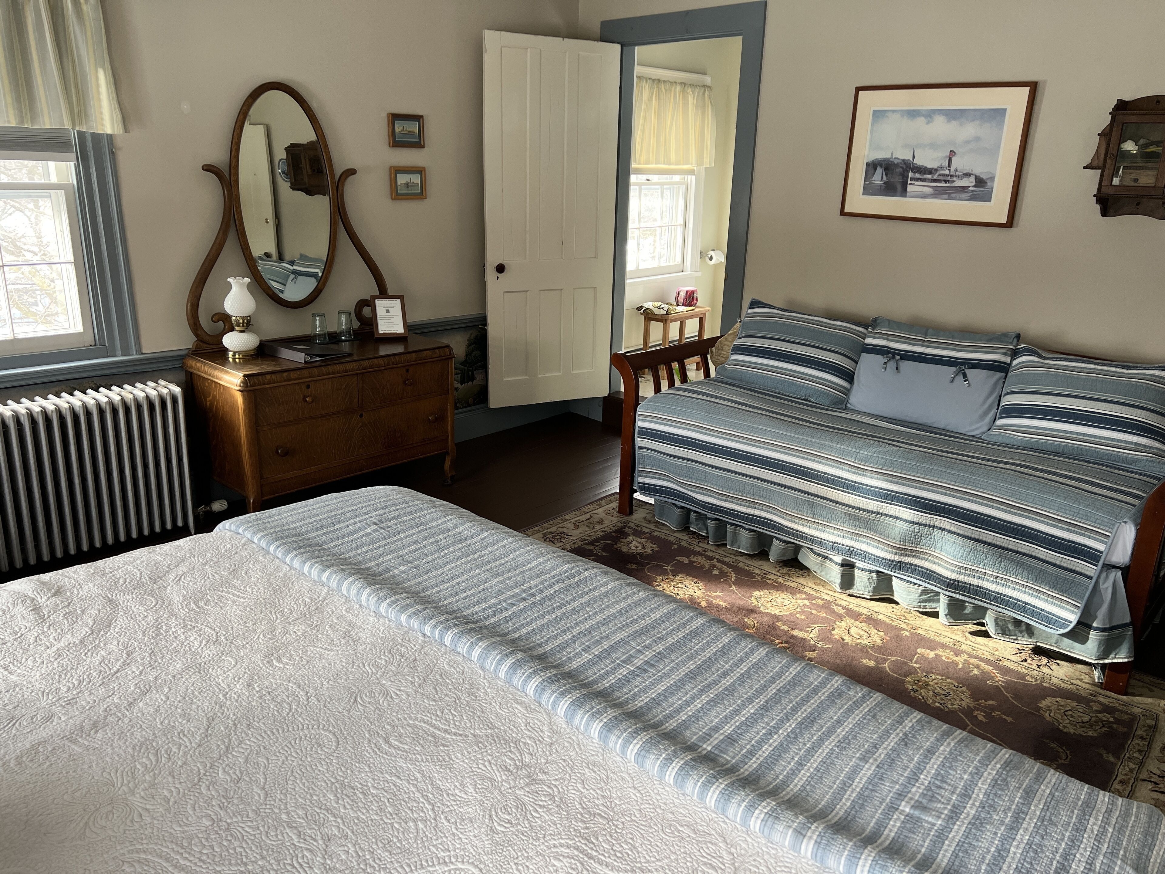 Un dormitorio con cama, cómoda, espejo y ventana con cortinas.