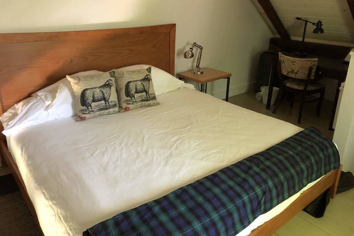 A bed with a wooden headboard, two pillows with sheep designs, a small bedside table with a lamp, and a chair in a corner.