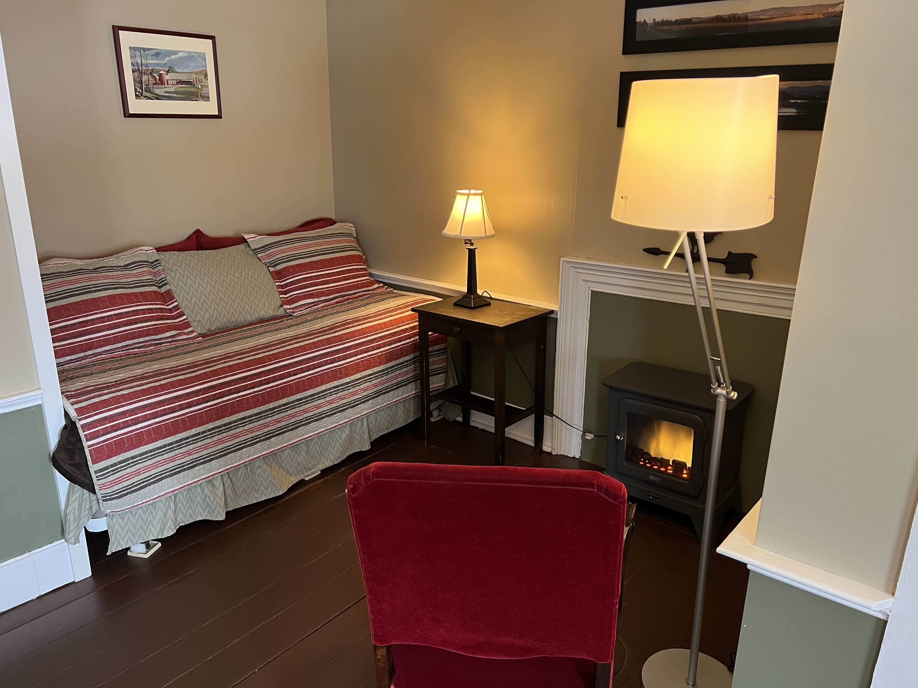 Une pièce confortable avec un lit, un fauteuil rouge, une lampe et une cheminée.