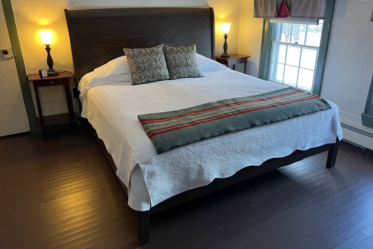A neatly made bed with patterned pillows, a bedside table with a lamp, and a window with a view.