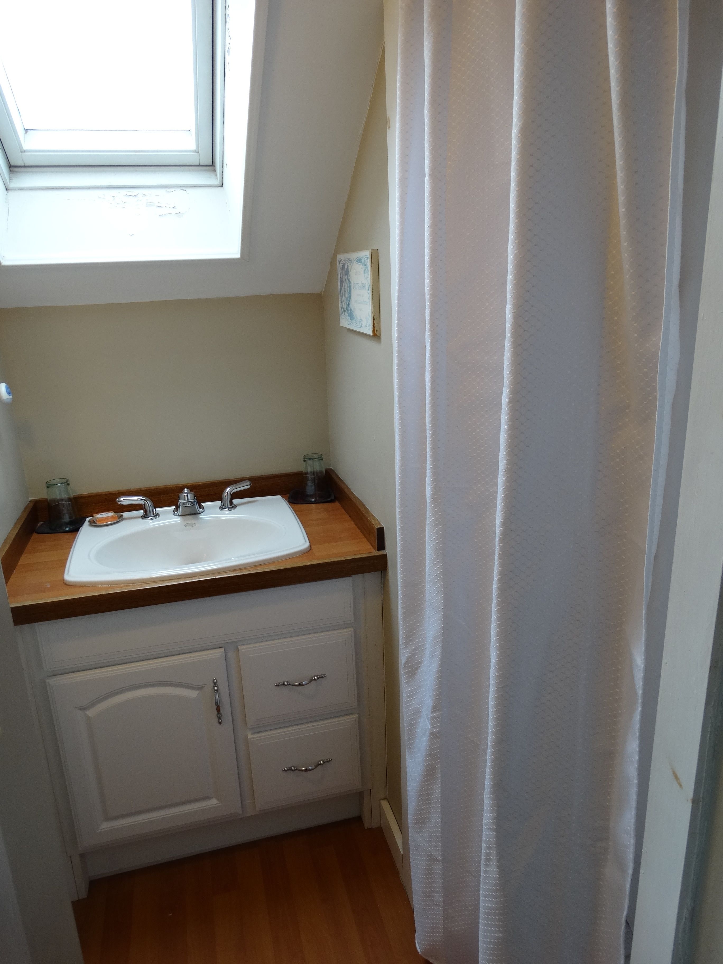 Un baño pequeño con un lavamanos blanco, encimera de madera y un tragaluz.