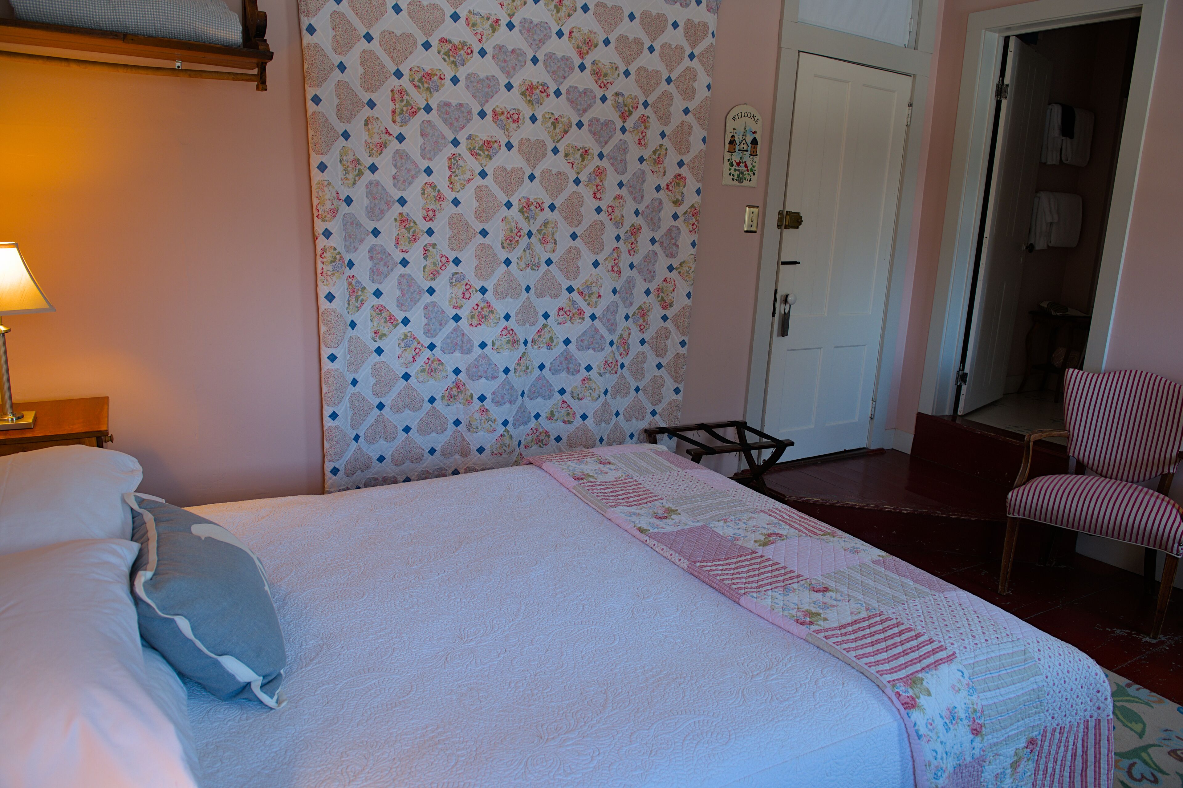 Une chambre à coucher avec un lit, des oreillers, une couette, une chaise et une porte.