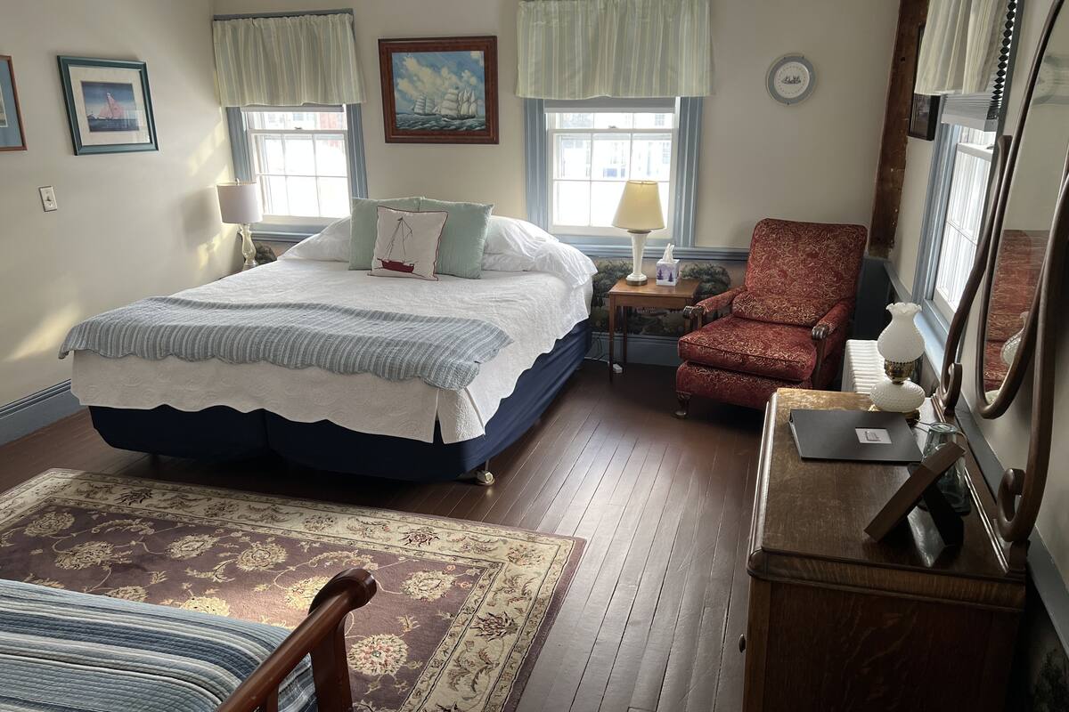 A bedroom with a large bed, a chair, a desk, and a mirror.