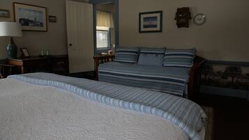 A bedroom with a large bed, a smaller bed, a nightstand, a lamp, and a window.