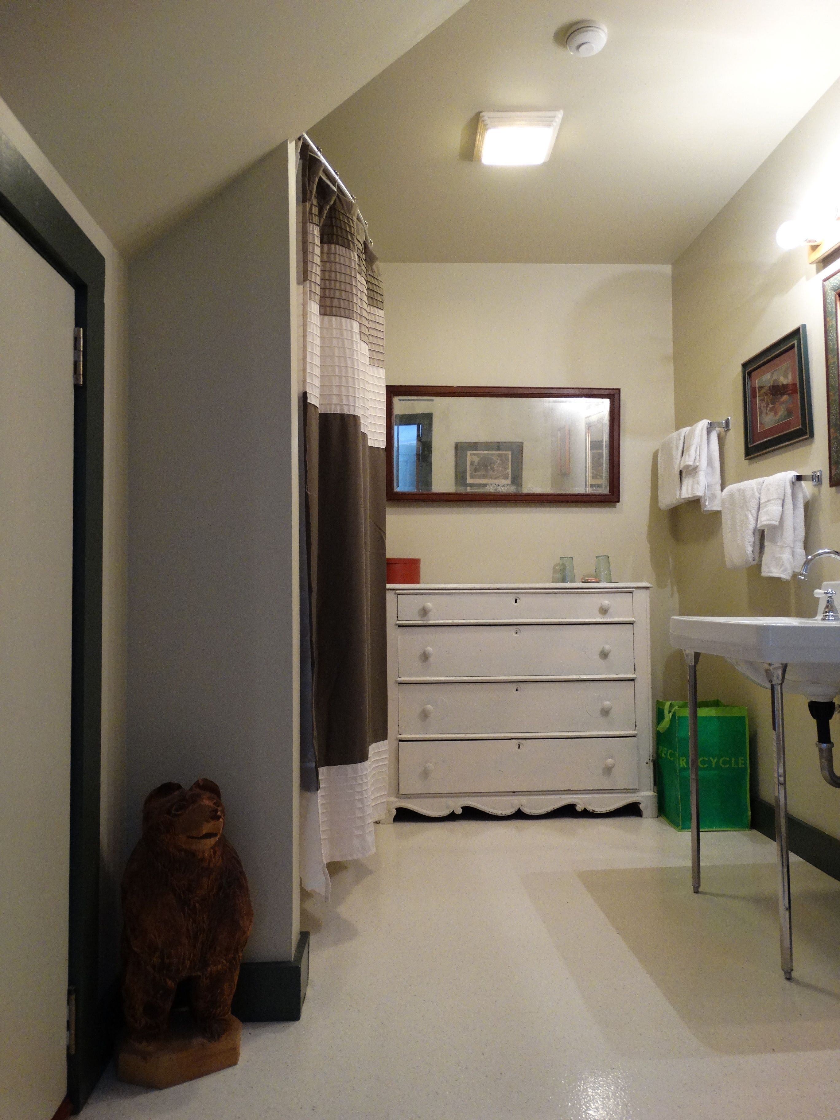 A bathroom with a white vanity, a mirror, a green bag, and a teddy bear statue.