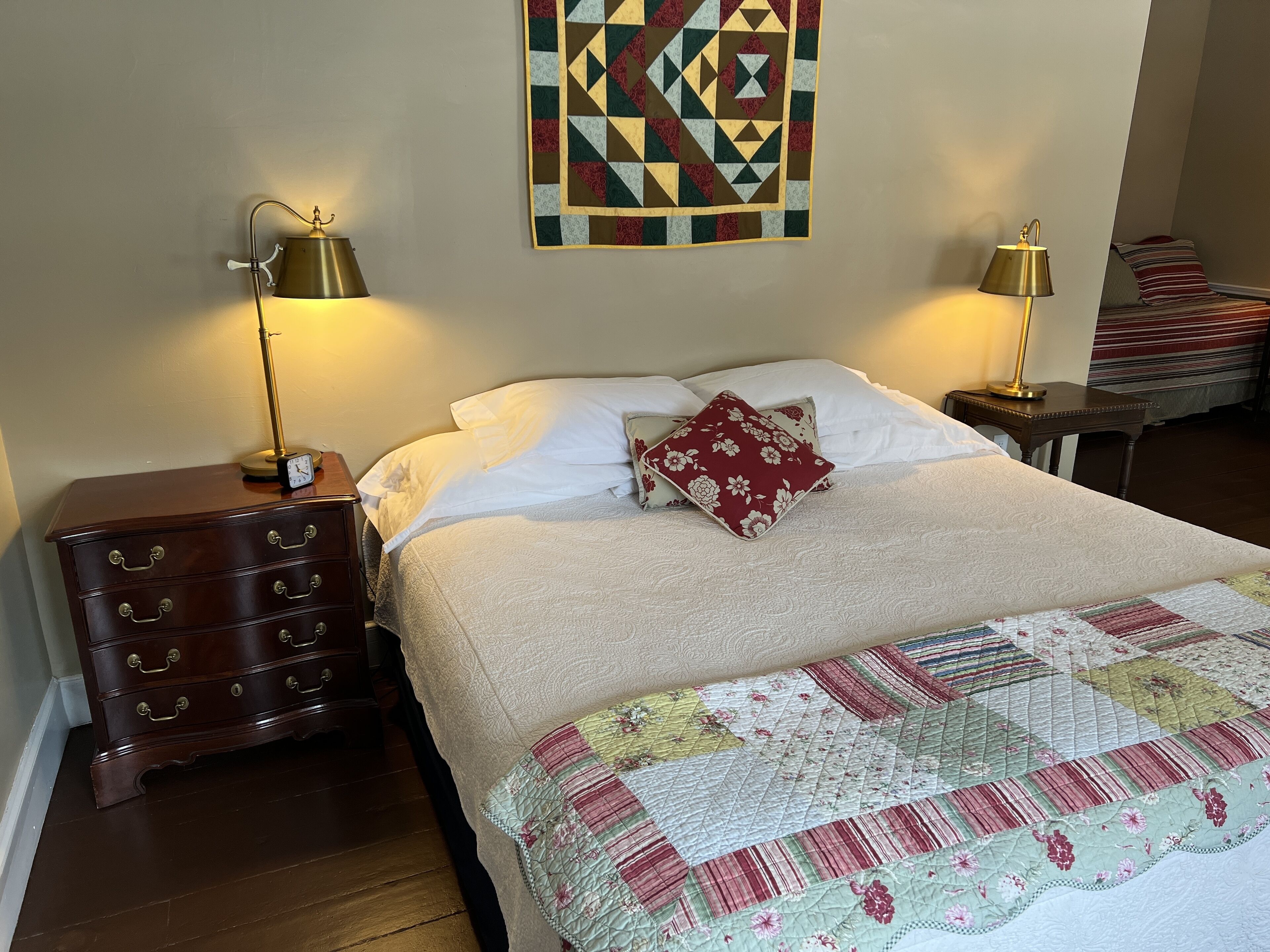 Een slaapkamer met een bed, twee bedlampen, een houten dressoir en een sprei.
