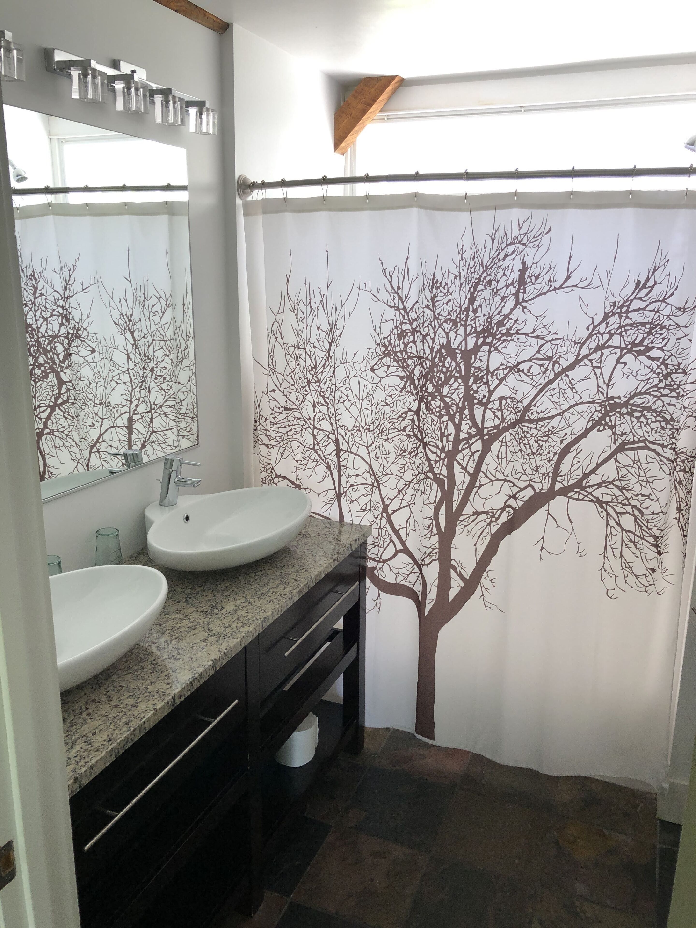 A bathroom with two sinks, a mirror, and a shower curtain with a tree design.