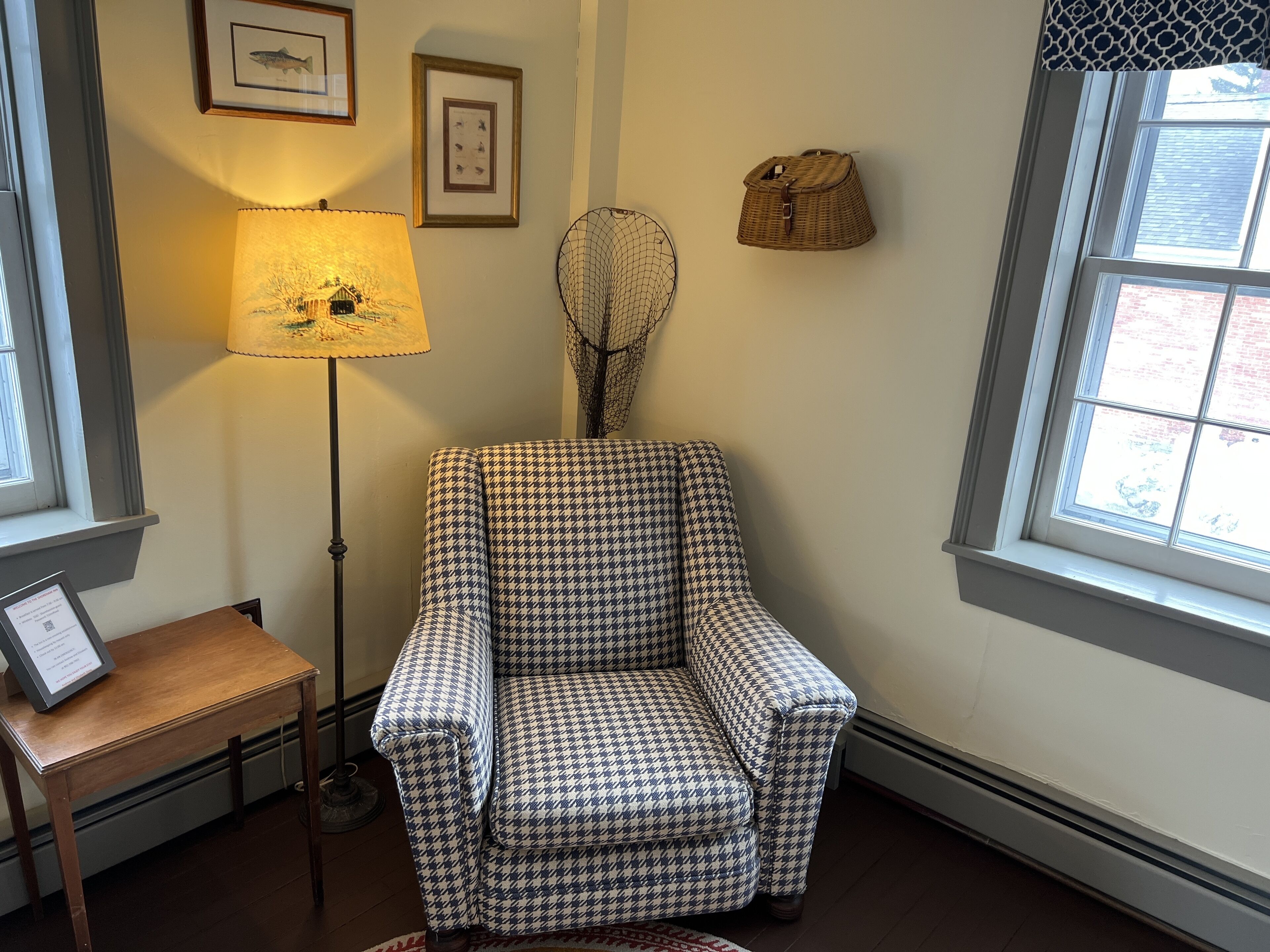 A houndstooth-patterned armchair in a room with a lamp, framed pictures, and a window.