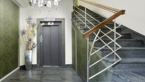 Un interior moderno con una escalera, una zona de recepción y un jarrón decorativo con flores.