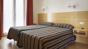Habitación de hotel con dos camas, cabecero de madera, mesitas de noche y una ventana con cortinas.
