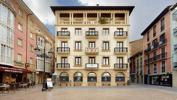 Un edificio de varios pisos con una entrada central, balcones y locales comerciales en la planta baja.