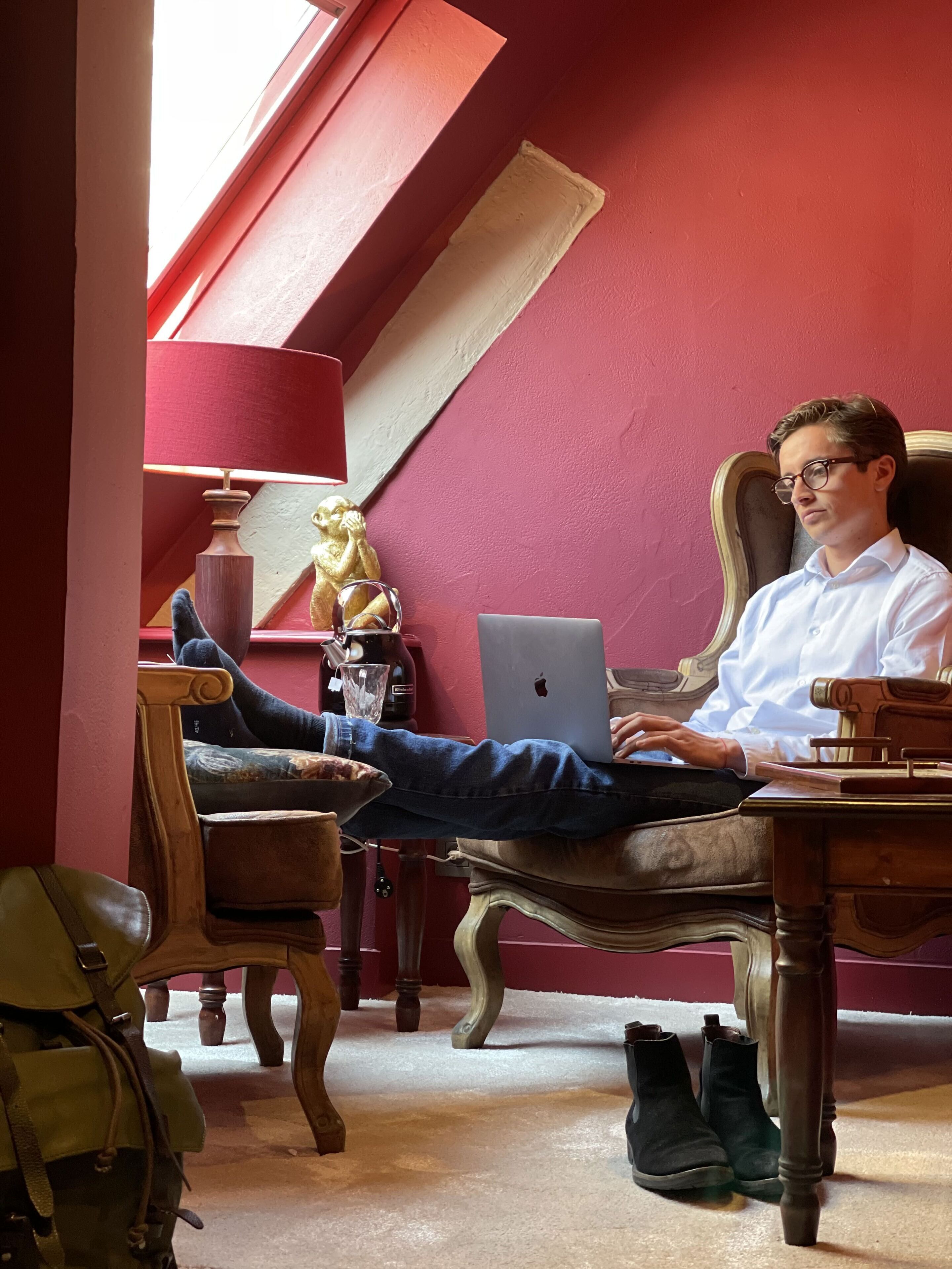 A person sitting on a wooden chair in a room with red walls and a slanted ceiling.