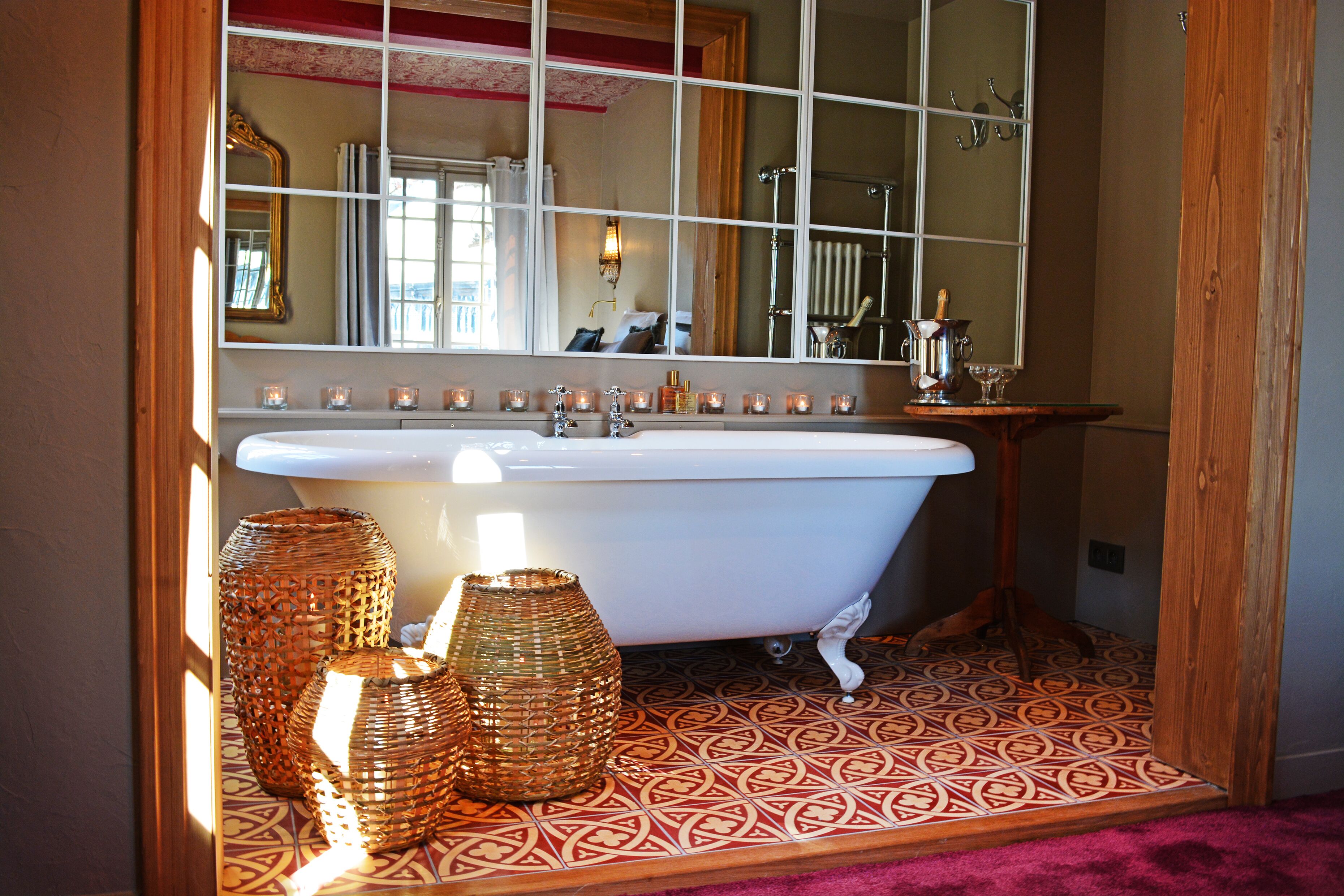 A bathroom with a freestanding bathtub, a large mirror, and a patterned floor.