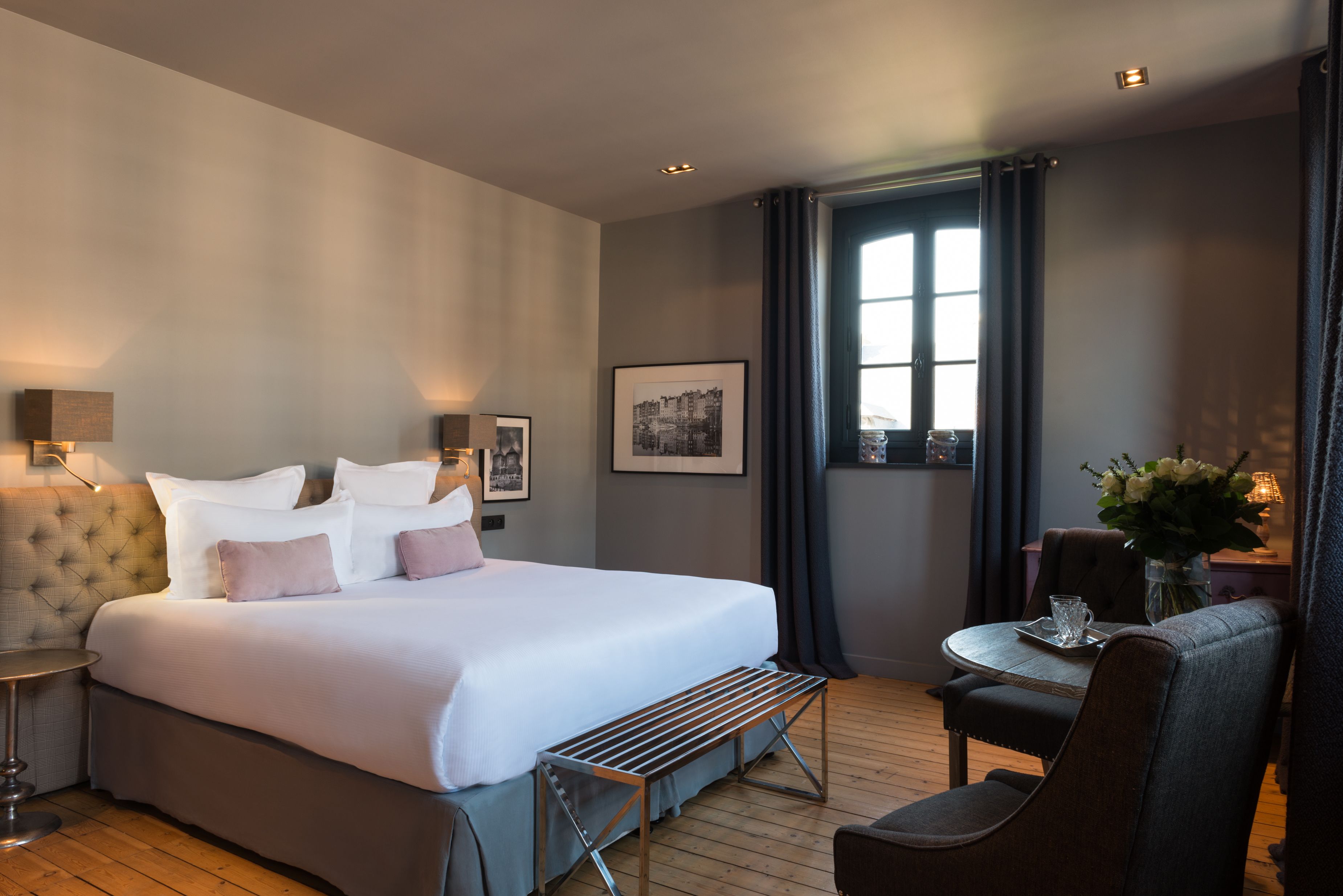A hotel room with a large bed, bedside tables, a small table with a vase of flowers, and a chair.