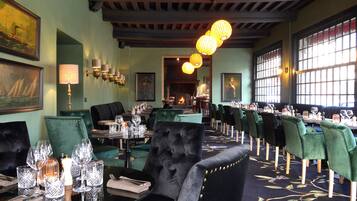 Un restaurante con sillas tapizadas de verde, una silla de terciopelo negro, y una mesa preparada con copas de vino y una vela.
