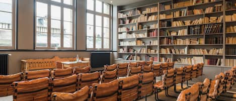 Una biblioteca con hileras de sillones de cuero, grandes ventanales y estanterías llenas de libros.