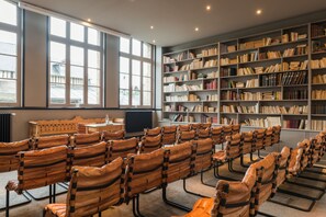 Une bibliothèque avec des rangées de fauteuils en cuir, de grandes fenêtres et des étagères remplies de livres.