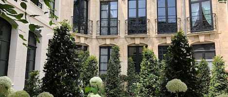 Un edificio con varias ventanas y balcones, rodeado de vegetación exuberante y flores blancas.