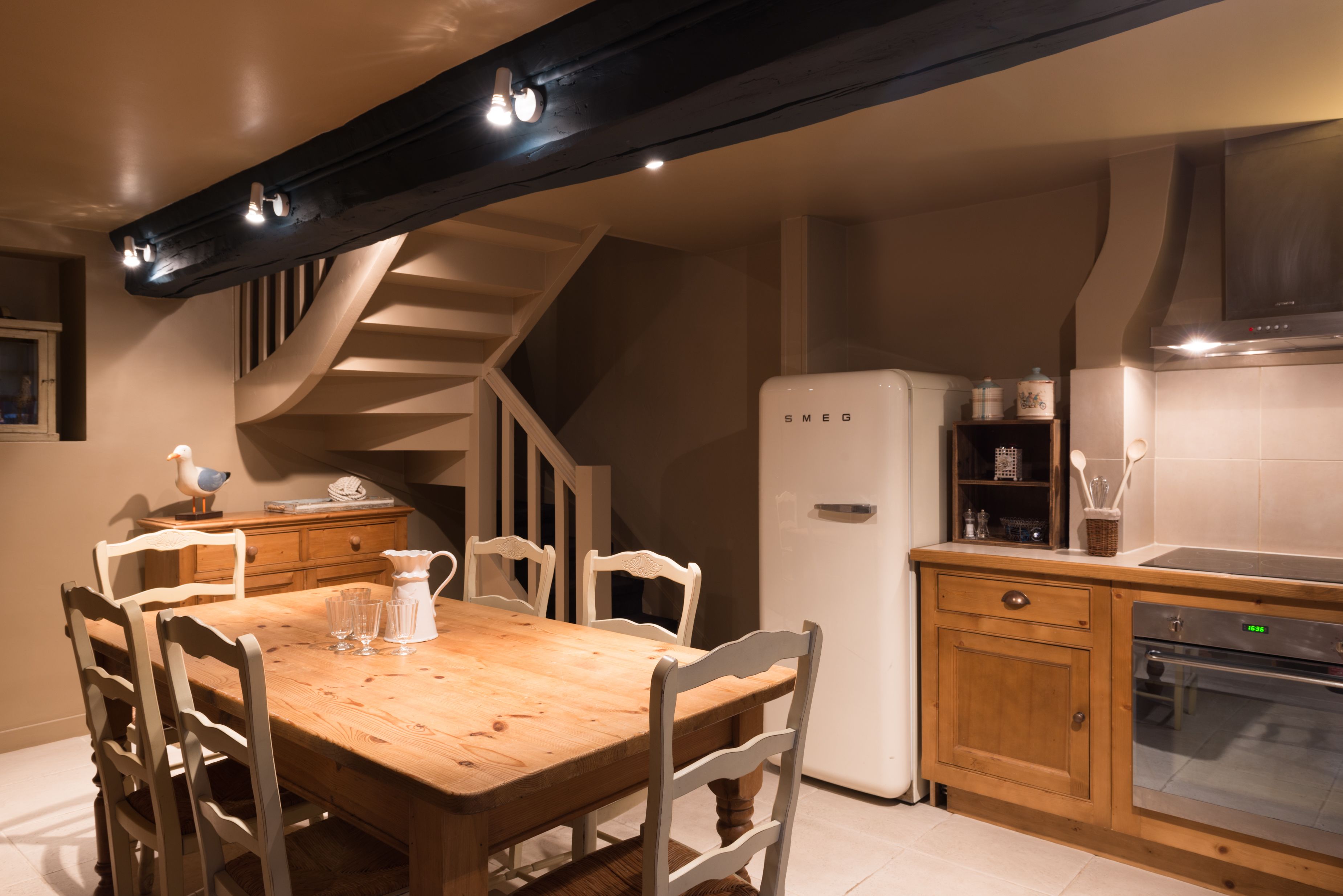 A kitchen with a wooden table, white chairs, a white refrigerator, and a built-in oven.