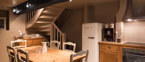 A kitchen with a wooden table, white chairs, a white refrigerator, and a built-in oven.