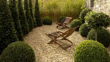 A garden with two wooden lounge chairs, neatly trimmed bushes, and a gravel path.