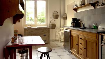 A kitchen with a wooden table, stools, a dishwasher, and a window with baskets hanging on the wall.