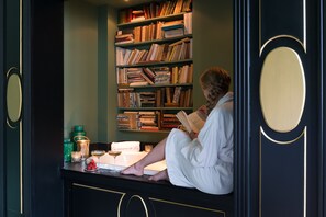 Iemand leest in een kamer met een boekenkast, een glas wijn en een kaars op een tafel.