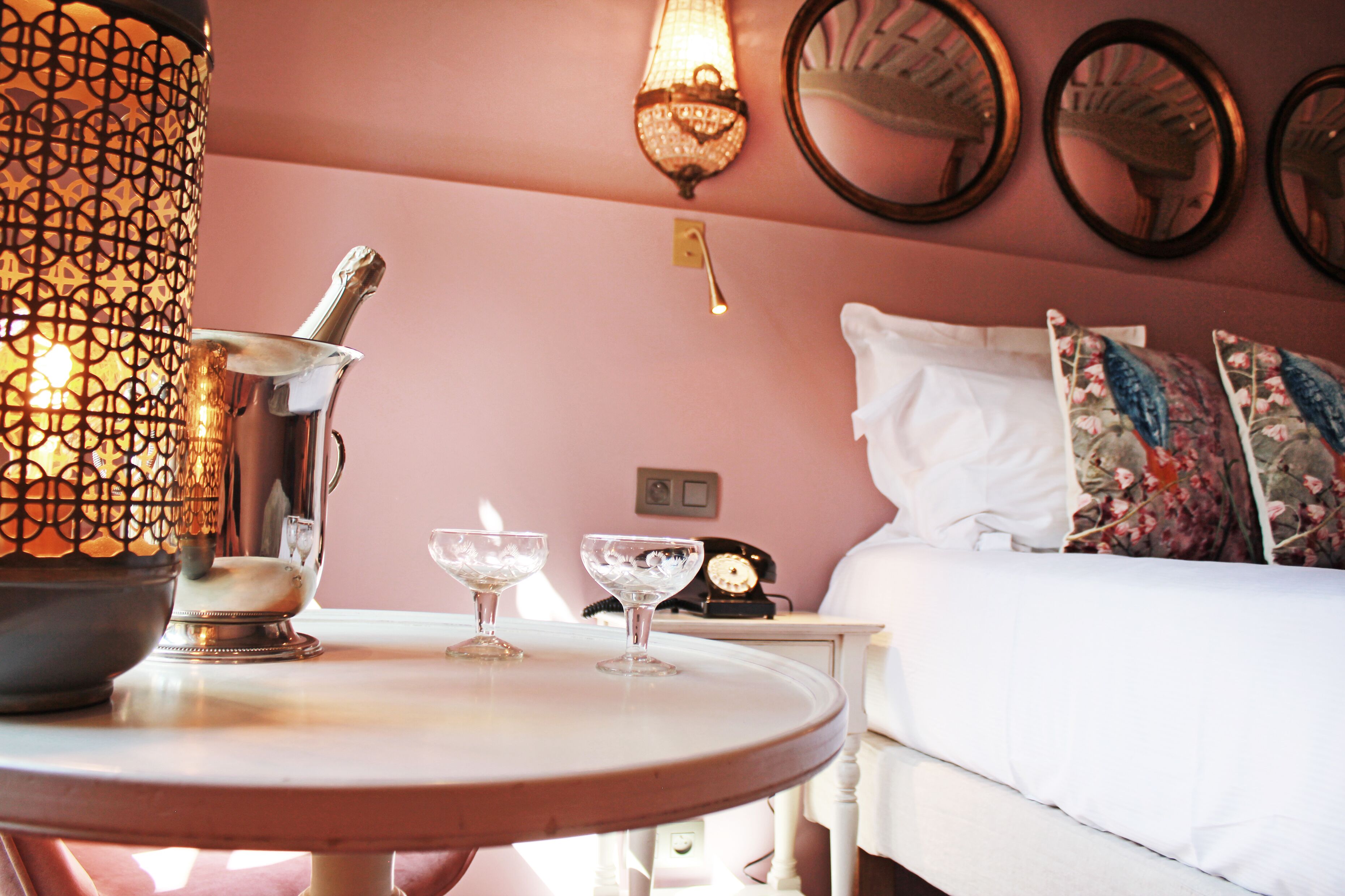 A room with a bed, a bedside table with a lamp, a clock, and decorative pillows.