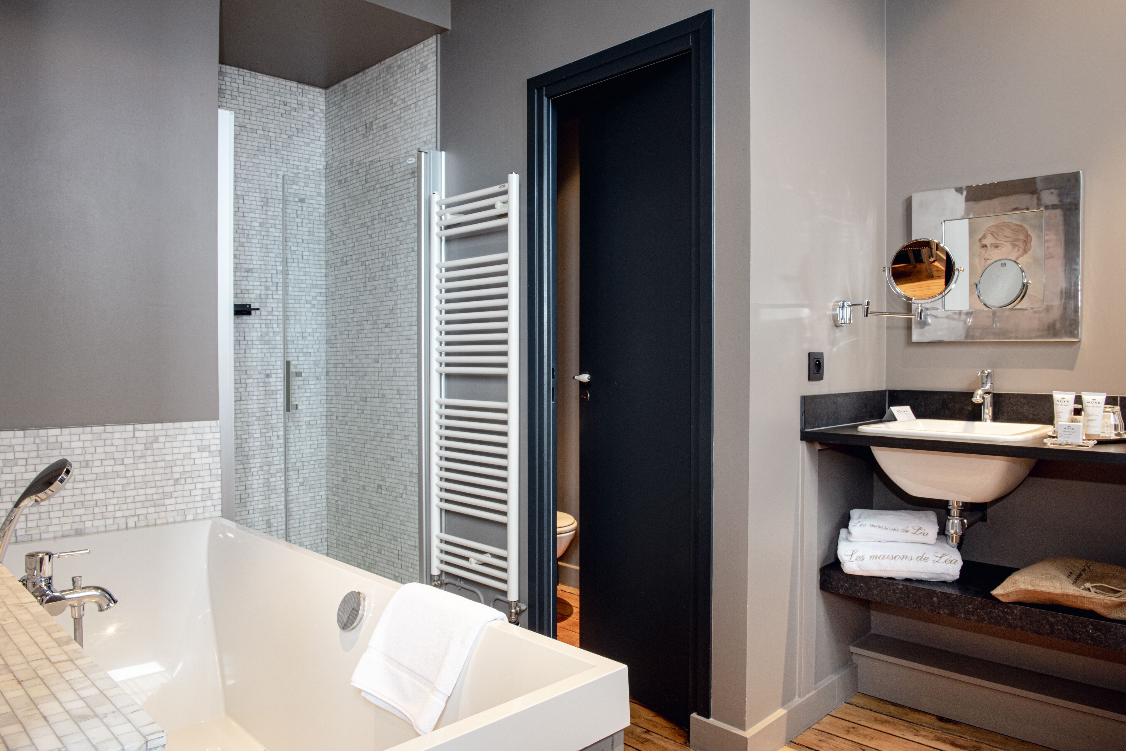 A modern bathroom with a white bathtub, a black door, a white sink, and a towel rack.