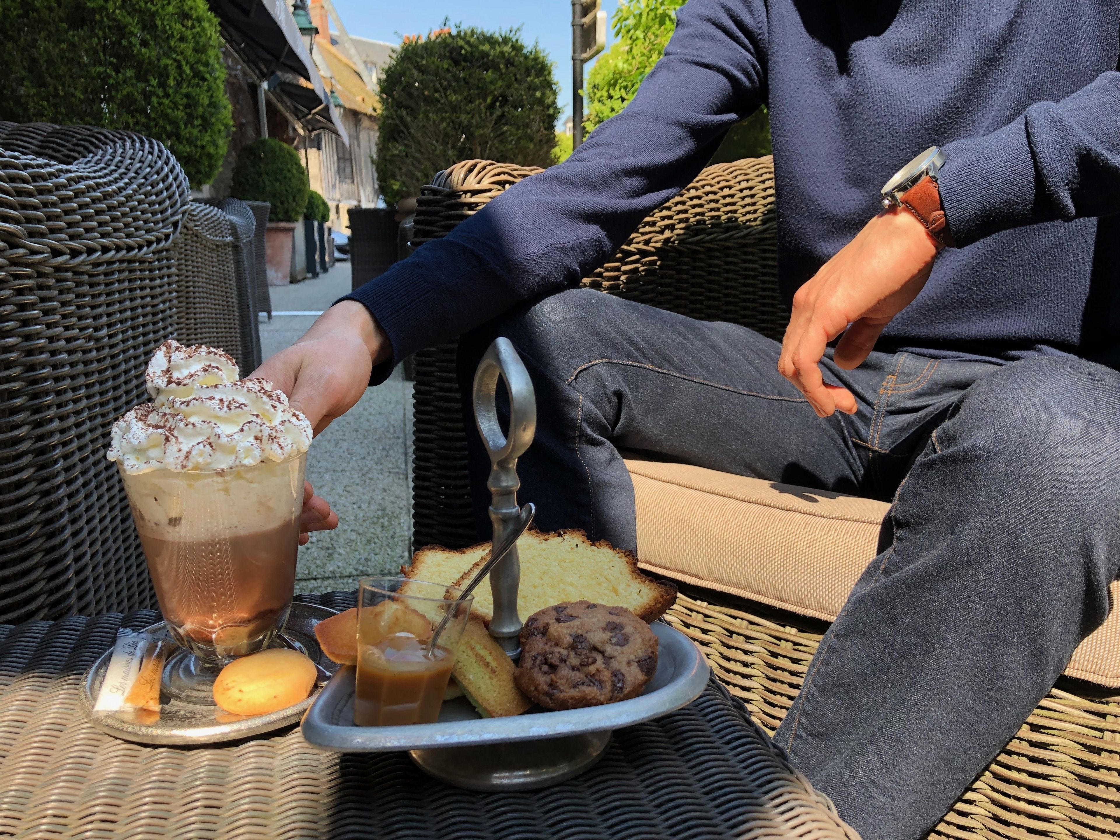 A person sitting on a wicker chair outdoors with a plate of food and a drink.